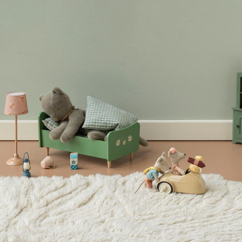 Stoffmaus schiebt Spielzeugauto mit Maus. Plüschkatze liegt im Bett.