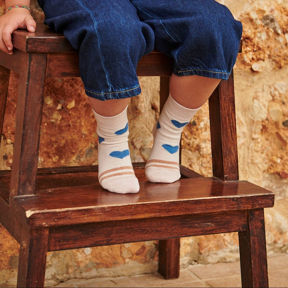 Kind auf einem Holzhocker mit cremerosa Strümpfe von mp Kids mit blauen Herzen
