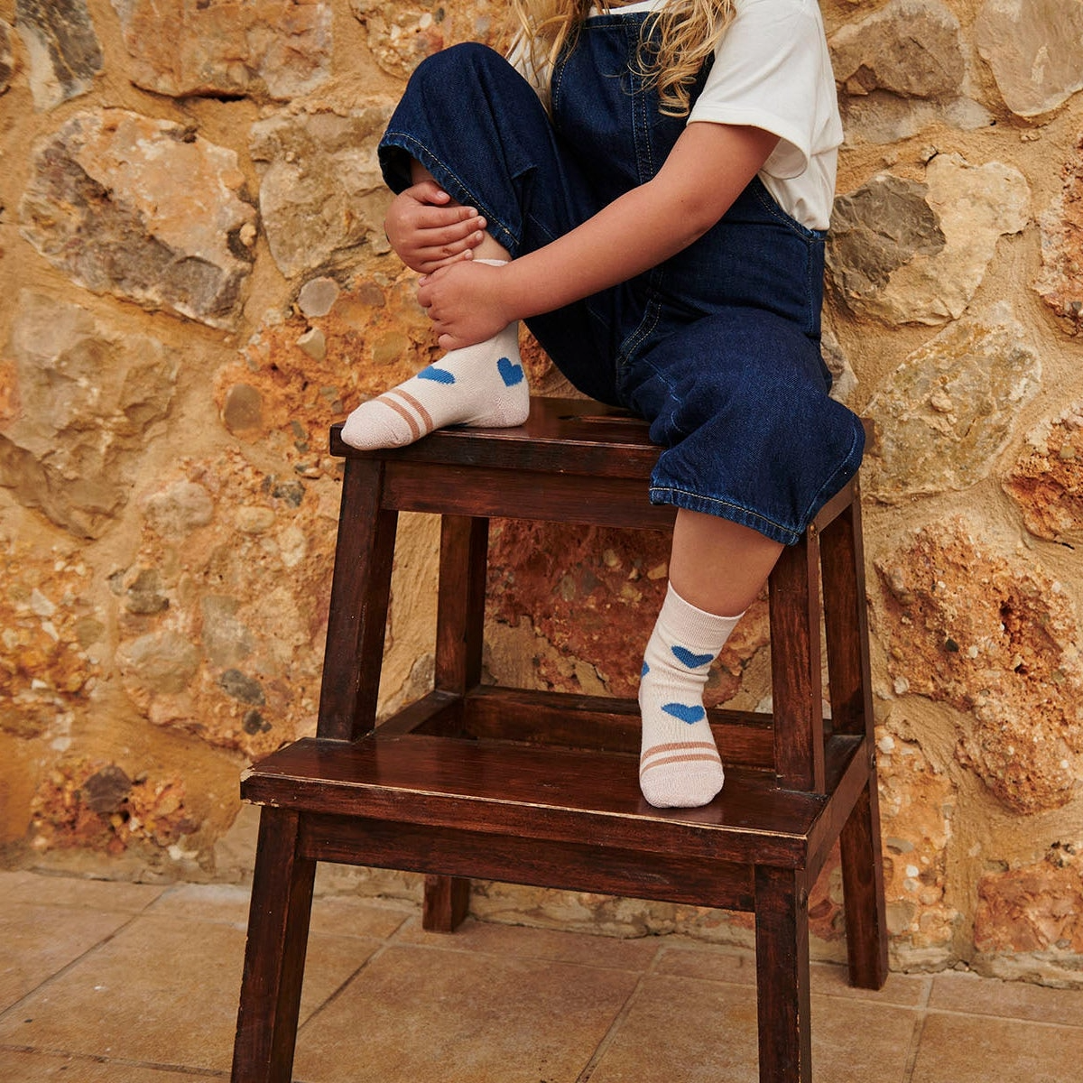 Kind sitzt auf Hocker mit cremerosa Strümpfe von mp Kids mit blauen Herzen